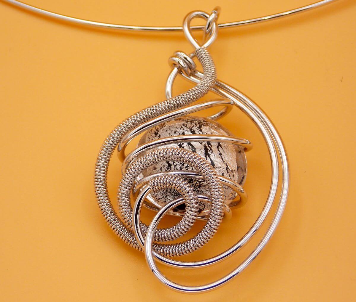 detail of swirling silver tone rhodium metal and silver bead pendant on tan background